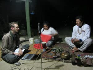 Lukas Kristo recording two curanderos in Peru. It is night, all three are sitting on the ground with a microphone in the middle and some instruments on the ground.